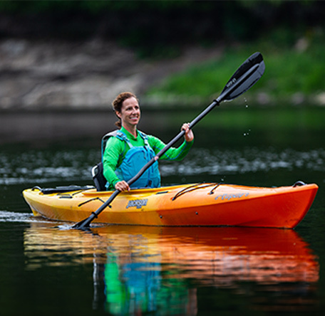 Happy woman paddling a Tupelo Jackson Kayak on a peaceful lake
