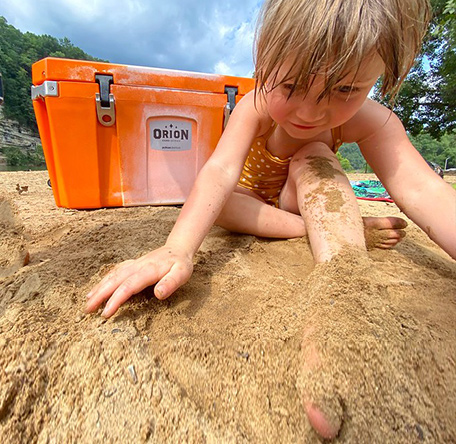happy young girl playing in sand in front of an orion cooler
