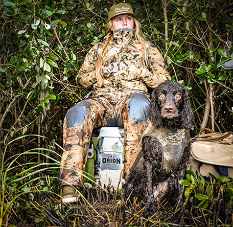 huntress sitting on an orion cooler with her boykin spaniel beside her