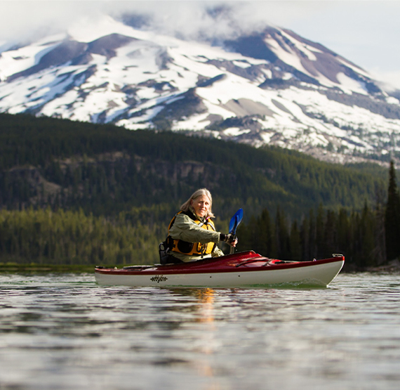 woman paddles across a serene lake scene in an Eddyline Kayak