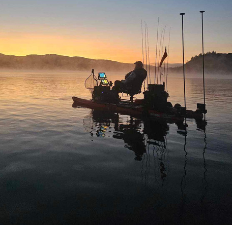 angler at sunrise in their blue sky boatworks kayak with rods and motors silhouetted