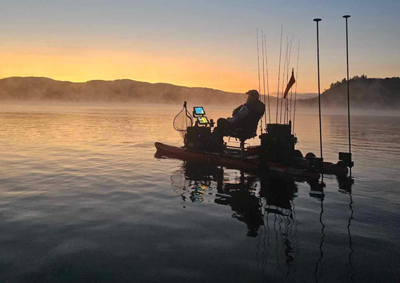 angler at sunrise in their blue sky boatworks kayak with rods and motors silhouetted