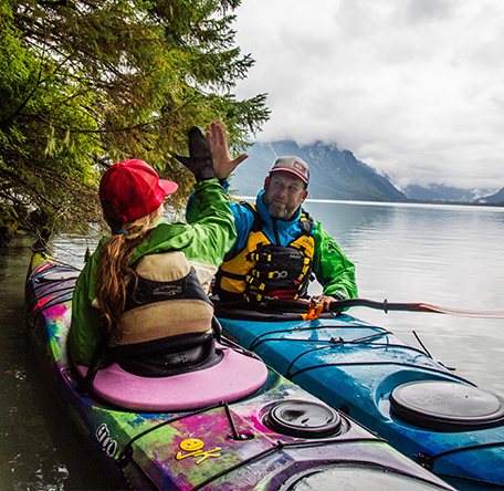 father and daugher high fiving from their jackson kayak journeys on a beautiful lake with mist rising in front of the mountains