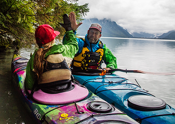 father and daugher high fiving from their jackson kayak journeys on a beautiful lake with mist rising in front of the mountains