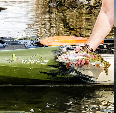 angler holding a trout in front of the Jackson Kayak Mayfly kayak logo