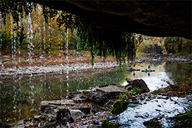 paddlers on a river with a dripping overhang in the foreground