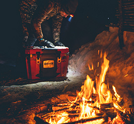 Person looking around an Orion Cooler next to a fire.