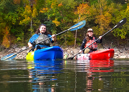Two people paddling kayaks in a fall scene.
